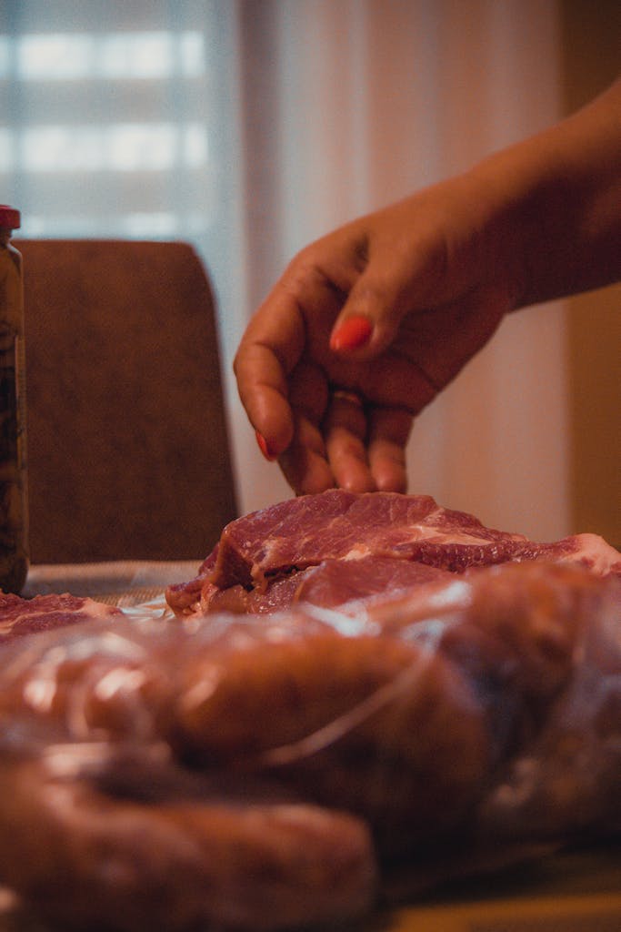 A close-up of a hand preparing raw meat pieces indoors. Perfect for culinary and food industry use.